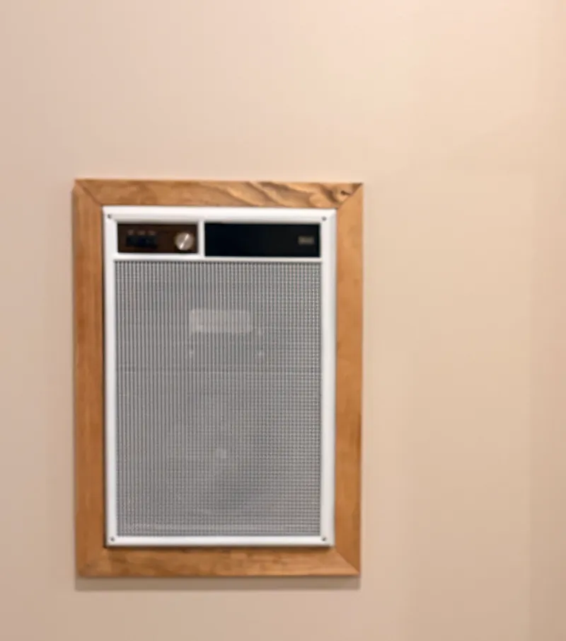 The wall heater framed in stained wood on a painted wall