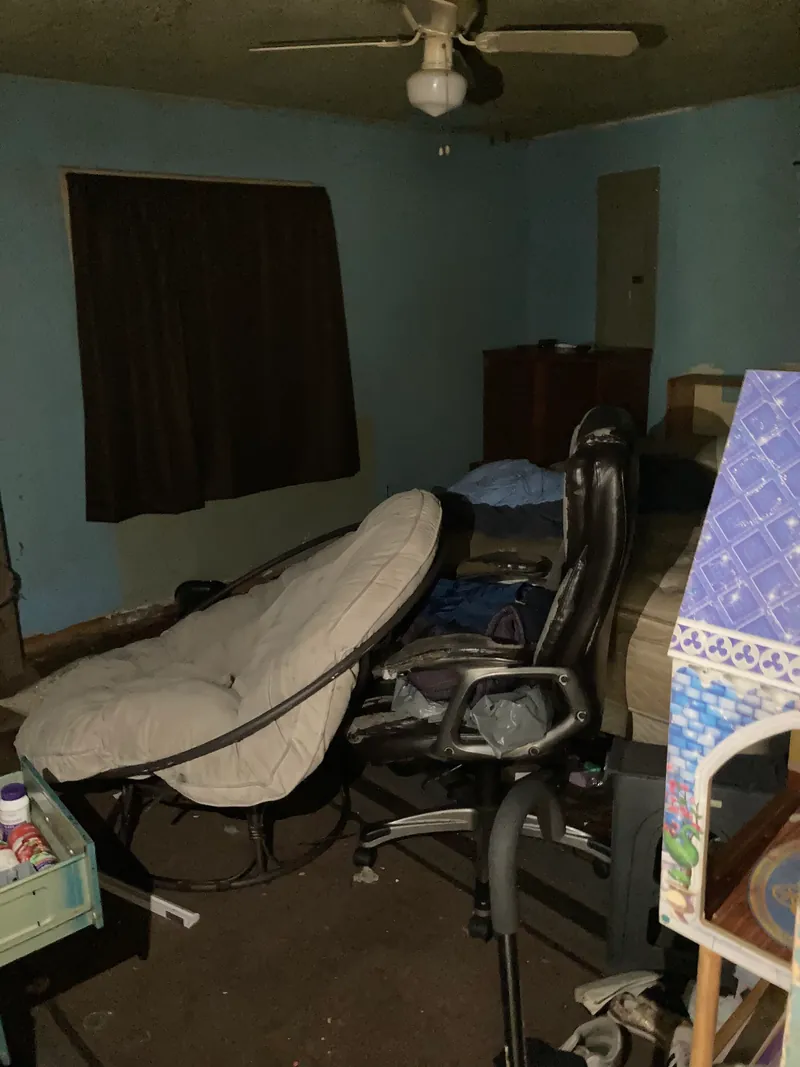 Bedroom with blue walls, dark curtains and a chair among belongings