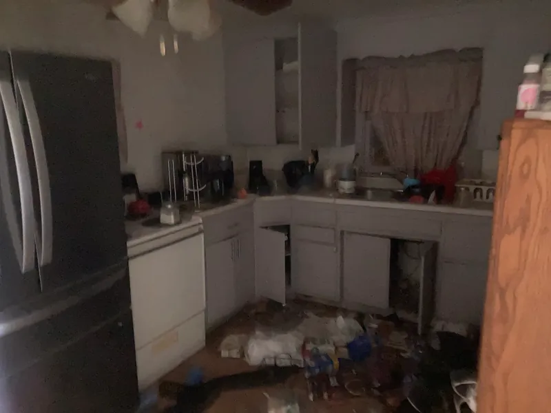 Cluttered kitchen with a refrigerator, open cabinets and trash on the floor