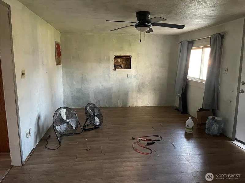 Emptied living room with a dark plank floor, a ceiling fan and two floor fans