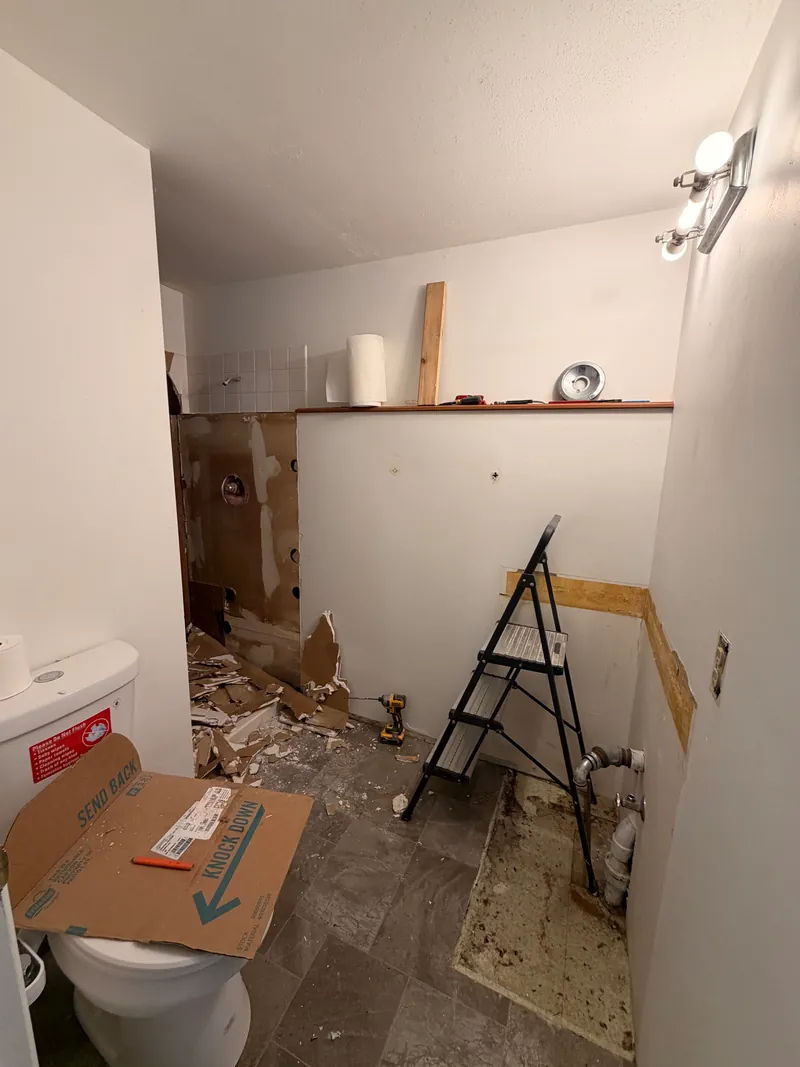 Bathroom during demolition with a ladder, exposed wall and debris