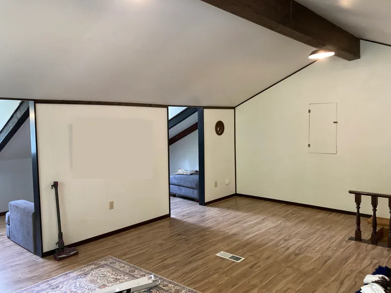 Finished loft with a dark wood box beam, white walls with dark trim and luxury vinyl plank flooring