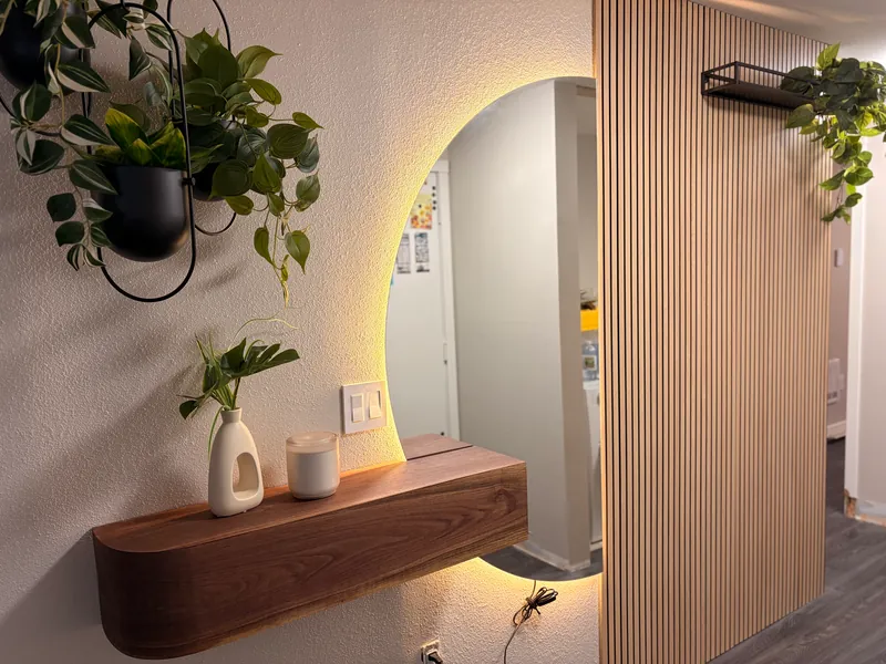 Vertical wood slat wall beside a backlit round mirror and a floating walnut shelf