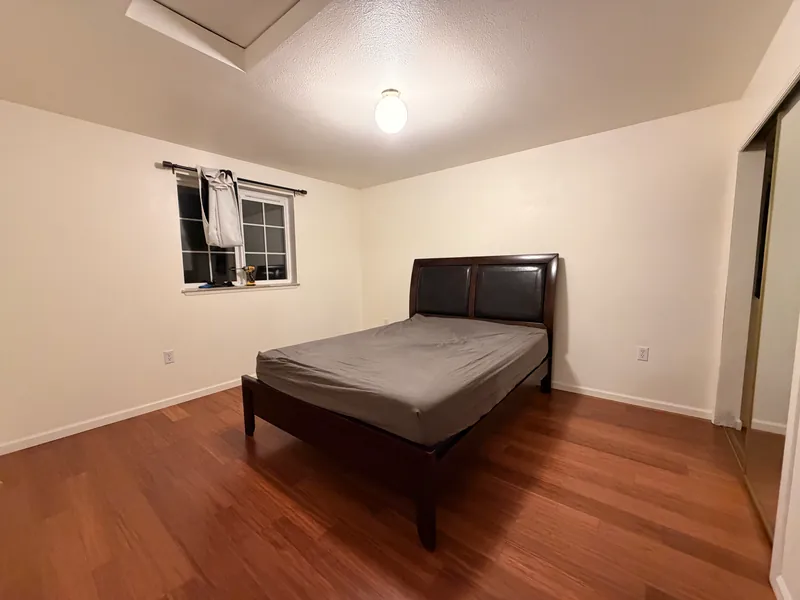 Bedroom with new warm-toned plank flooring and a dark bed frame