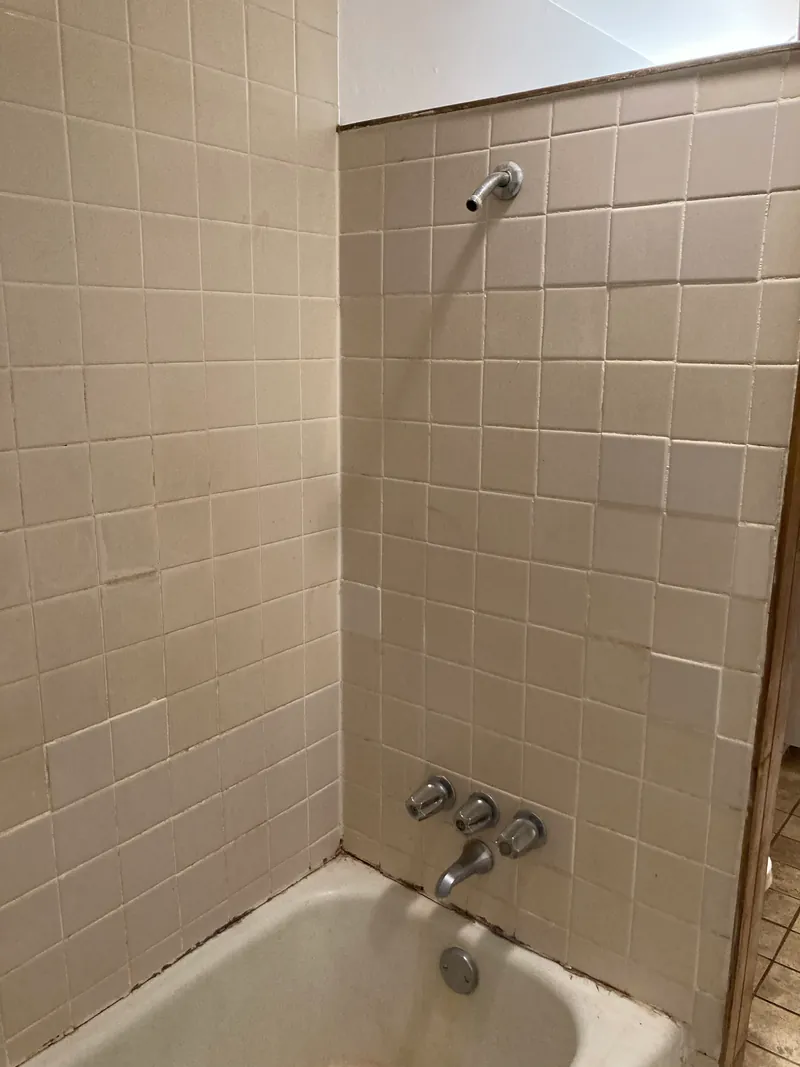 Bathtub with worn tile surround and outdated fixtures before renovation