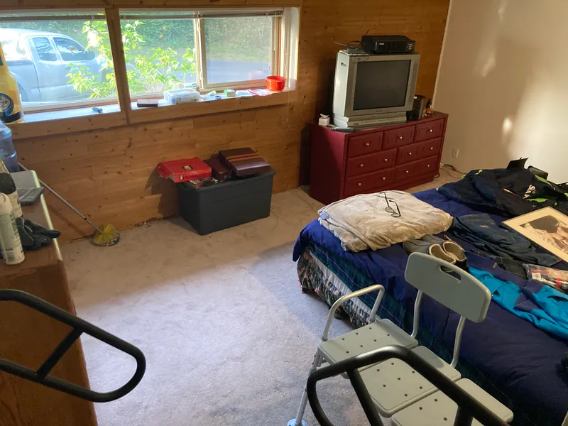 Bedroom with carpet, a cluttered bed, a dresser and a television before the work