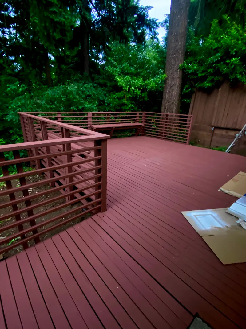 Freshly repainted red deck with a horizontal-slat railing surrounded by trees