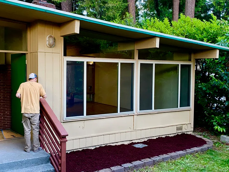 Painter prepping the exterior siding beside a green door and a railing