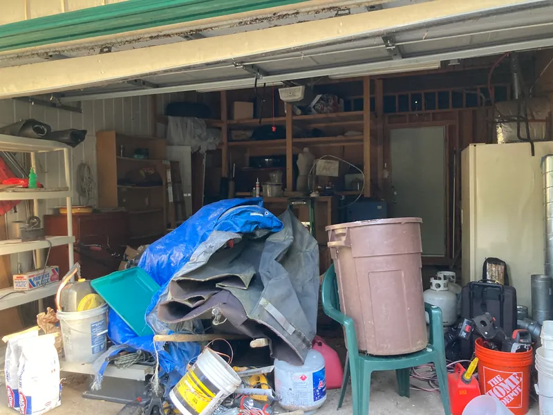 Garage full of stored items, a blue tarp, buckets and shelving before cleanout