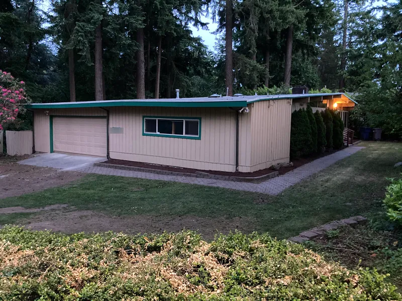 Single-story home with tan siding and green trim at dusk, with a freshly mulched bed along the walkway