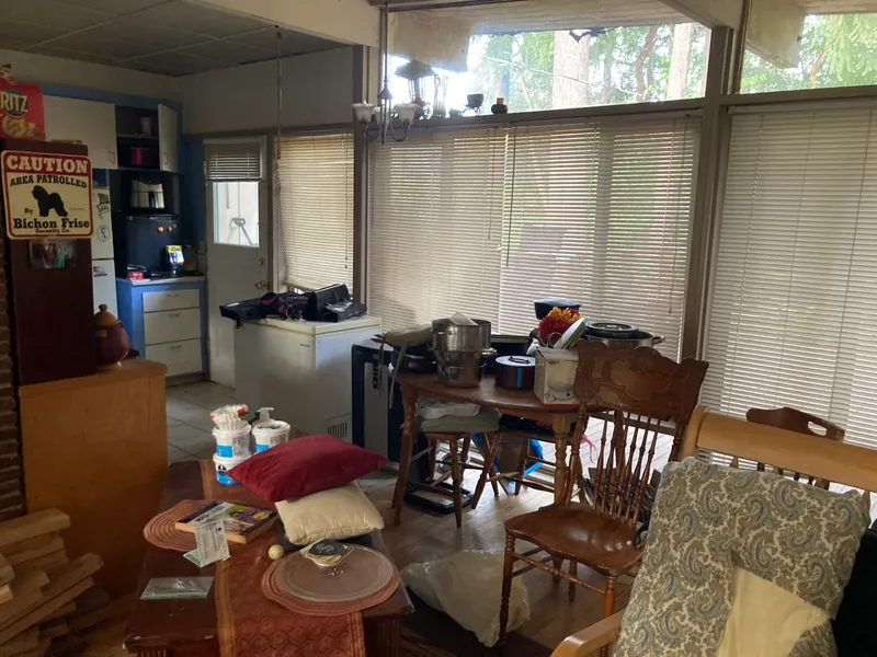 Living area cluttered with furniture, a dining table and boxes before the work
