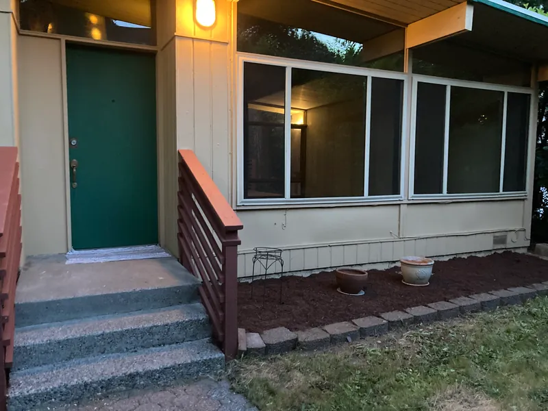Front entry with a green door, repainted siding, large windows and a freshly mulched bed