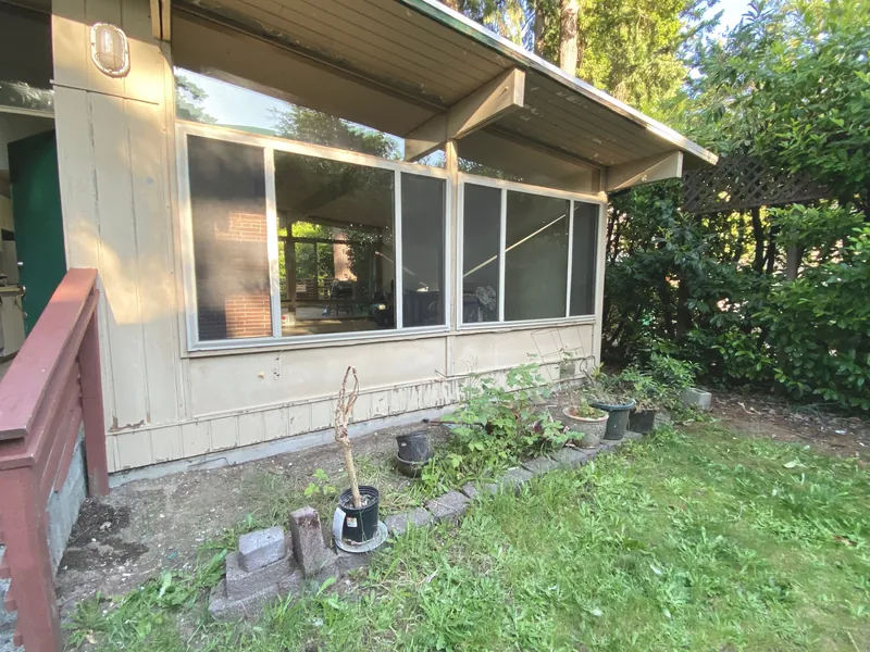 Side of the house with a weathered tan wall, large windows and an overgrown planting bed before the work