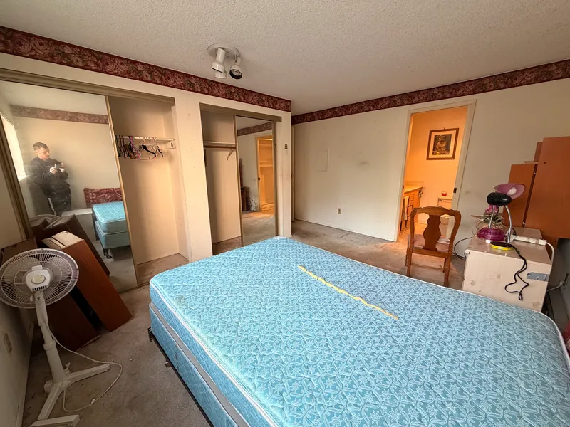 Bedroom with a wallpaper border, mirrored closet doors and worn carpet before renovation