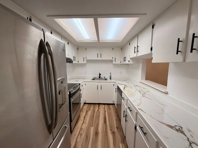 Renovated galley kitchen with white cabinets, black pulls, a marble-look countertop and new plank flooring